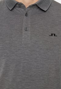 Szara koszulka polo wykonana z miękkiego materiału, z kołnierzykiem, trzema guzikami i subtelnym czarnym logo na piersi.