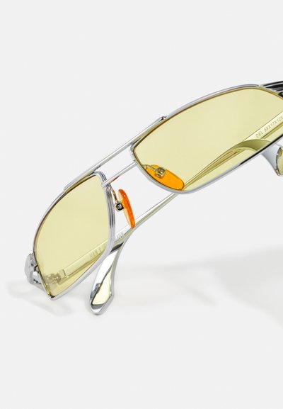 Yellow-tinted sunglasses with silver metal frame. Features a unique bridge design and orange detailing on the adjustable nosepiece.