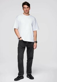 Biała, oversize koszulka w połączeniu z ciemnoszarymi jeansami. Czarne trampki dopełniają strój, tworząc swobodny i relaksujący wygląd.