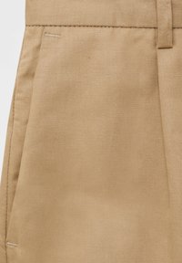 Tissu beige avec une texture diagonale côtelée subtile, présentant une coupe droite et des coutures soigneusement finies. Deux poches latérales visibles.