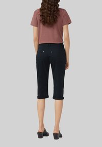 Dunkelblaue, kniehohe Hosen mit umgeschlagenen Säumen, kombiniert mit einem kurzärmeligen Top in staubigem Rosé. Dazu schwarze Schuhe mit Blockabsatz.