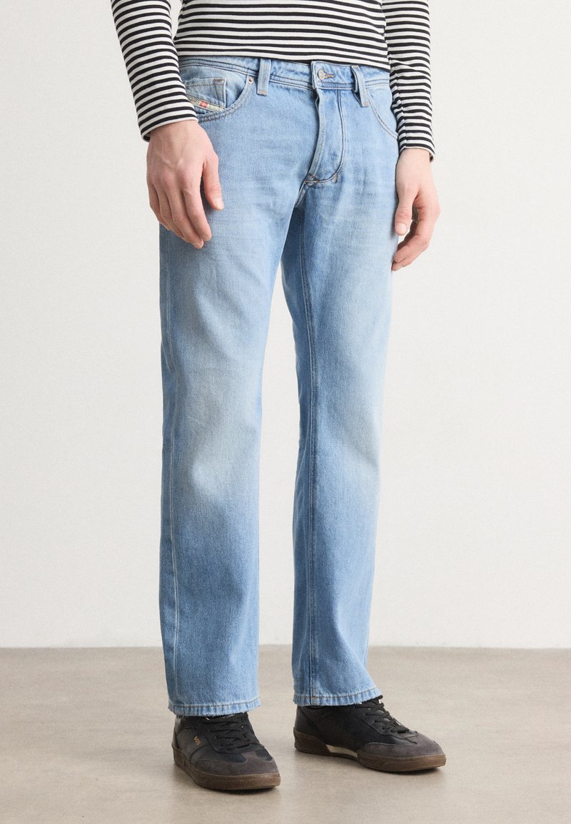 Helle blaue Denim-Jeans mit geradem Schnitt, ausgestattet mit einem klassischen Fünf-Taschen-Design und einem Reißverschluss. Tragen mit schwarzen Sneakers.