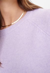 Helles Lavendel-Pullover mit Rundhalsausschnitt, gerippten Kanten und weicher Textur. Eine glatte goldene Halskette liegt an dem Ausschnitt.