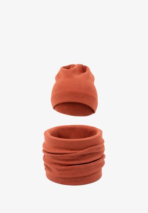 Prążkowana, dziergana czapka w kolorze rdzy oraz pasujący komin, pokazane osobno na białym tle.