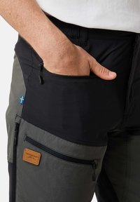 Zwarte en olijfgroene hikingbroek met meerdere ritszakken, textuurstof en een leren merkembleem. Bevat een accent van de Zweedse vlag.