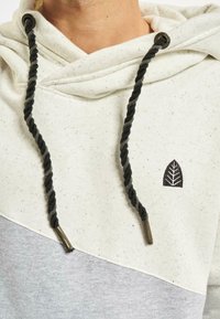 Hooded sweatshirt in light cream and gray, featuring a twisted black drawstring, embroidered leaf logo, and speckled fabric texture.