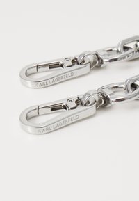 Cadena de metal con dos clips en tono plateado, grabados con "KARL LAGERFELD", que exhiben un acabado pulido y eslabones robustos.