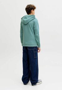 Hoodie in licht teal, katoenmix, met geribbelde boorden. Gecombineerd met losvallende donkere spijkerbroek met zijzakken.