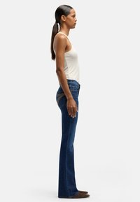 Blå utsvängda jeans med midjemått, sydda detaljer på bakfickorna och en mjuk denimstruktur. Kombinerade med ett figurnära linne.