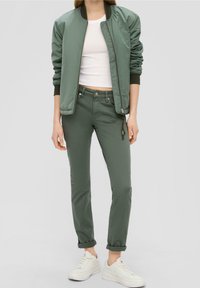 Chaqueta bomber verde con puños y cuello acanalados, combinada con pantalones ajustados verdes a juego y zapatillas blancas. Textura suave en toda la prenda.