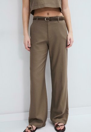 Person iført brune vidde bukser med høj talje og matchende bælte, croppet top og sorte åbne sandaler med guldaccenter.