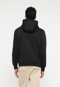 Schwarzer Hoodies mit einer großen, strukturierten Kapuze, aus weichem Material gefertigt. Mit gerippten Bündchen und Saum, in mittellanger Schnittform.
