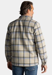 Beige geruite overhemd met blauwe en zwarte lijnen. Gemaakt van zachte stof, heeft knoopmanchetten en een klassieke kraag. Gezien vanaf de achterkant.