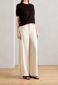 Černý pletený top s krátkým rukávem zkombinovaný s krémovými širokými kalhotami s hladkou texturou a minimalistickým designem, doplněný černými sandály.