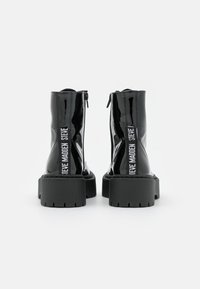 Bottines en cuir verni noir avec une semelle épaisse noire, dotées de fermetures éclair latérales et de la marque "STEVE MADDEN" en blanc sur les côtés.