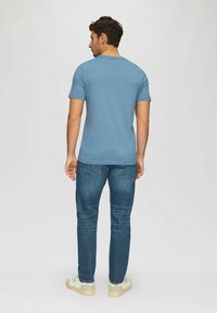 Helles blaues Kurzarm-T-Shirt, kombiniert mit dunklen Jeans, von hinten gezeigt. Das Outfit bietet ein lässiges Design und eine lockere Passform.