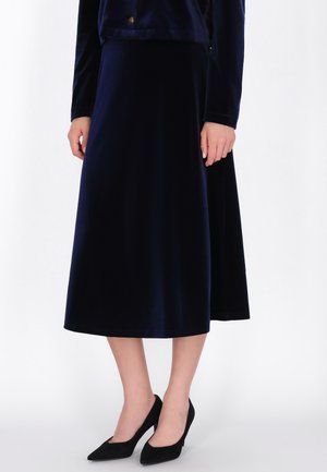 Modelo con una falda midi de terciopelo azul marino oscuro, una chaqueta a juego y zapatos negros de tacón con puntera puntiaguda.
