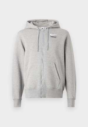 Sweat à capuche zippé gris avec cordon de serrage, poches avant et poignets côtelés. Arbore un logo Nike et le texte "ATHLETE" en noir. Fabriqué en tissu doux.