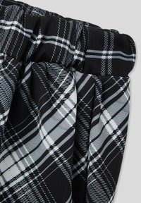 Tessuto a quadri in bianco e nero con dettaglio di vita elastica arricciata, che mostra motivi lineari diagonali e verticali.