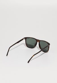 Ochelari de soare din tortoiseshell cu lentile de culoare verde închis, având o formă rectangulară și brațe subțiri, elegante. Detaliu cu logo clar pe ramă.