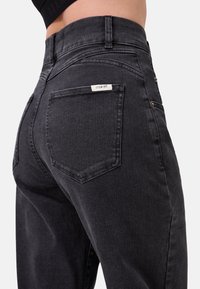 Jeans in denim nero con vita alta, dotati di due tasche posteriori, una piccola etichetta del marchio e una superficie liscia, leggermente texturizzata.
