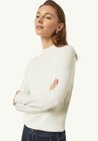 White ribbed sweater with a high neck and long sleeves, paired with dark jeans. Smooth texture and fitted design.