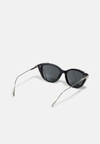 Mustad musta värvi cat-eye päikeseprillid hallide tumedate läätsedega, hõbedased metallist aktsendid templites ja sujuvad, kaarduvad käed. Siledad plastraamid.