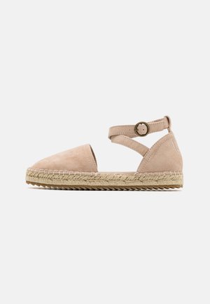 Espadrille en suède beige avec un bout arrondi et une bride à la cheville, dotée d'une semelle en jute tissée et de détails de couture subtils le long du bord.