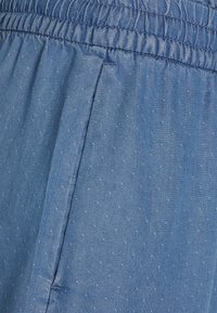 Modrá látka se jemným tečkovaným vzorem, elastický pas a postranní šev. Materiál se jeví jako lehký a texturovaný.