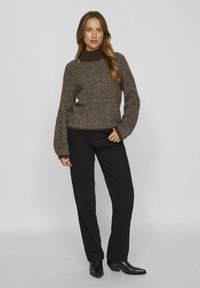 Maglione a trama a spina di pesce marrone e bianco con colletto alto, abbinato a pantaloni neri e stivali neri a punta. Tessuto morbido e texturizzato.