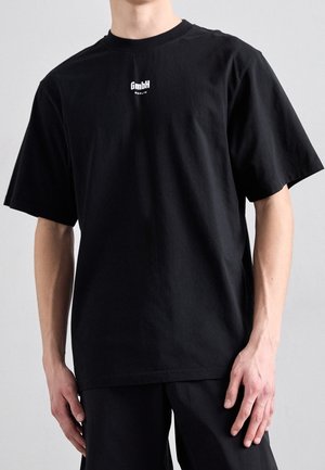 Black cotton t-shirt with a relaxed fit, short sleeves, and a small white logo on the chest. Simple design with no additional patterns.