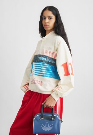 Felpa crema con strisce orizzontali blu e rosse, con la scritta "VERADO SPIKERS" e il logo "adidas". Pantaloni tuta rossi e una borsa blu con logo.