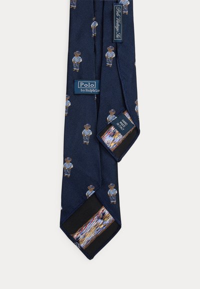 Γραβάτα από μπλε μετάξι ναυτικού χρώματος με επαναλαμβανόμενα κεντημένα αρκουδάκια που φοράνε μπλε σακάκι και καπέλο, με την ετικέτα "Polo by Ralph Lauren", χειροποίητη στην Ιταλία.