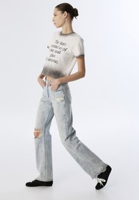 Witte en grijze ombre t-shirt met tekst, gecombineerd met lichtgewassen flared jeans met scheurdetails. Zwarte sneakers maken de look compleet.