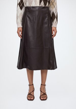 Persoon die een donkerbruine leren midi-rok draagt, bruine sandalen met hoge hakken en bandjes, en een beige argyle trui.