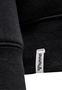 Svart sweatshirt med en mjuk textur, med en synlig etikett på fållen. Tyget har ett sl ätt vävt mönster.