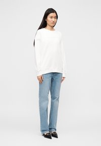 Λευκό βαμβακερό φούτερ με κεντημένο λογότυπο, άνετη γραμμή· συνδυασμένο με ανοιχτό μπλε τζιν παντελόνι· μαύρα παπούτσια με μυτερή μύτη.