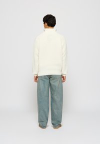 Hvit, teksturert genser med høy krage, med senkede skuldre og ribbede mansjetter, kombinert med lyseblå baggy jeans.