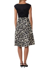 Haut à manches courtes noir associé à une jupe évasée longueur genoux avec une base crème et un motif léopard noir audacieux. Talons noirs.
