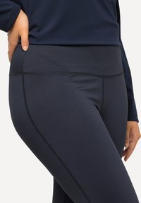 Leggings blu navy realizzati in un tessuto liscio ed elasticizzato con un alto punto vita, caratterizzati da cuciture piatte e senza motivi o accessori visibili.