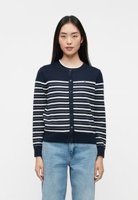 Ναυτικό κασκόλ με οριζόντιες λευκές ρίγες, στρογγυλή λαιμόκοψη και κούμπωμα μπροστά, κατασκευασμένο από μαλακό πλεκτό υλικό.