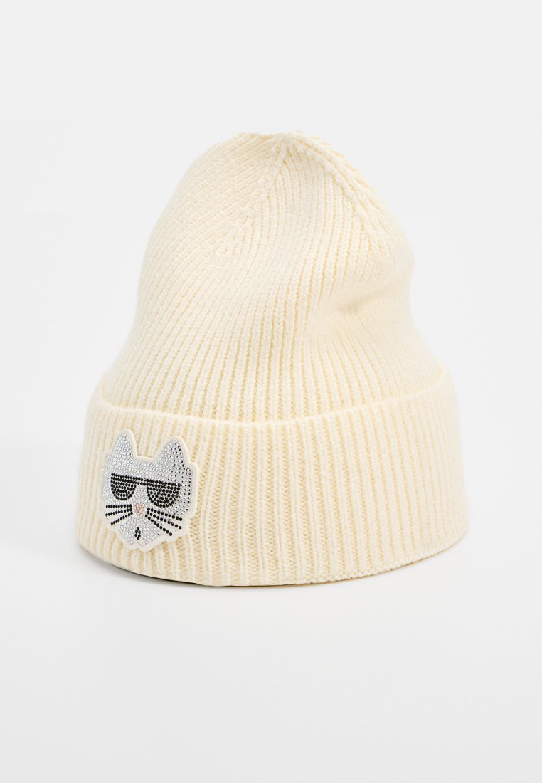 Häkelmütze in Cremefarbe mit geripptem Muster. Besitzt ein Katzenmotiv mit Sonnenbrille, verziert mit silbernen und schwarzen Details.