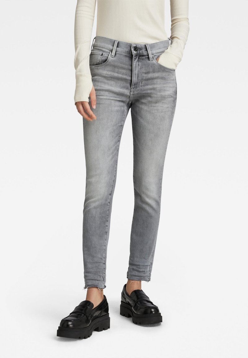 Jeans de mezclilla gris con una forma ajustada, diseño de cinco bolsillos y dobladillo deshilachado, combinados con mocasines negros de suela gruesa y una camiseta de manga larga blanca de canalé.