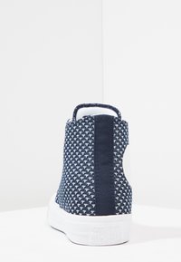 Tummansininen ja valkoinen kuvioitu korkeavartinen tennari, jossa on valkoinen kumipohja ja "Converse All Star" -logo kohokuvioituna kantapäässä.