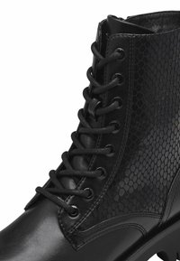 Bottines noires à lacets avec une tige en cuir lisse et un panneau texturé imitant le serpent, œillets ronds en argent et semelle épaisse.