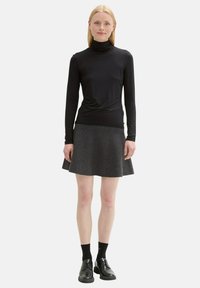 Schwarzes Langarm-Turtleneck-Shirt, kombiniert mit einem grauen, ausgestellten Rock. Strukturiertes Material mit glatter Oberfläche. Schwarze Schuhe und Socken runden das Outfit ab.