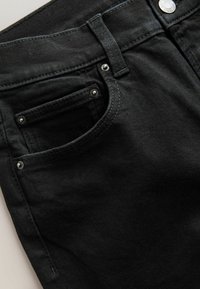 Mustad teksapüksid sujuva tekstuuriga, millel on münditasku, kontrastsete õmblustega ja hõbedaste detailidega vööl ja taskutel.