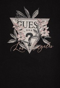 T-shirt en tissu noir mettant en avant un graphique triangulaire avec le texte "GUESS U.S.A." et "Los Angeles", rehaussé de motifs floraux et d'étincelles.