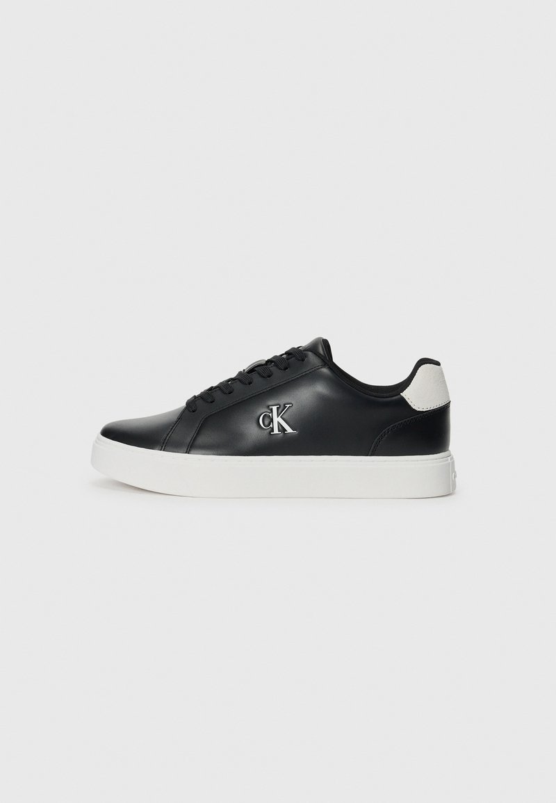 Zwarte leren sneaker met een witte rubberen zool, rond neus en vetersluiting. Voorzien van een zilveren logo aan de zijkant en een grijze accent aan de hiel.