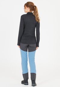 Zwarte langemouwen top met ribbeltextuur, gecombineerd met blauwe en grijze outdoor broeken met een twee-kleurig design en drukknoopsluitingen bij de enkels.